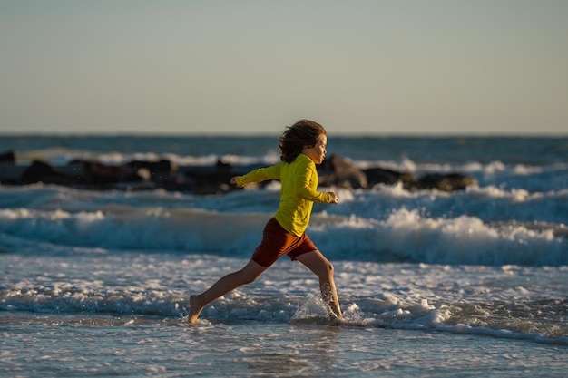 Criança correndo e brincando na praia tropical no verão garoto aproveita as férias de verão no mar garoto r