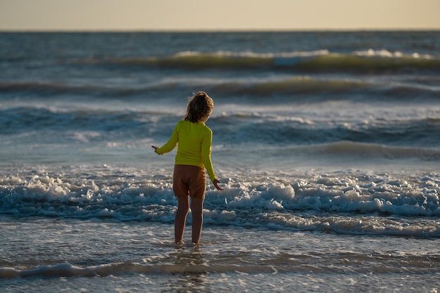 Criança correndo para a água do mar durante as férias de verão menino correndo ao longo do oceano criança na praia de verão