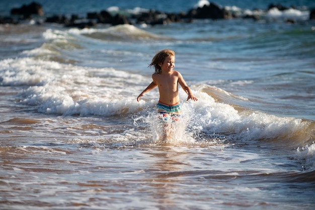 Criança correndo pela água perto da costa ao longo da praia do mar Um menino corre ao longo da costa do mar Resto das crianças nas férias de verão