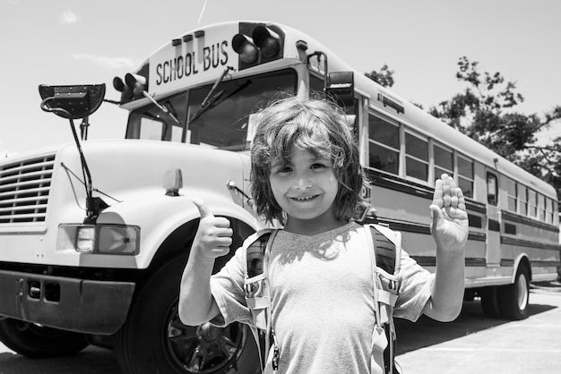 Criança da escola primária com saco no backgroung de ônibus escolar. Crianças de escola felizes.