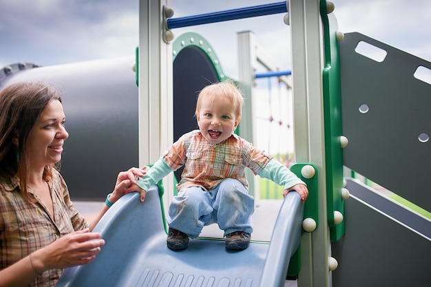 Criança de 1 ano de idade feliz brincando no playground com a mãe.