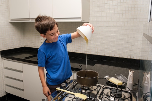 Criança de 8 anos na cozinha sorrindo e despejando leite condensado na panela para fazer brigadeiro