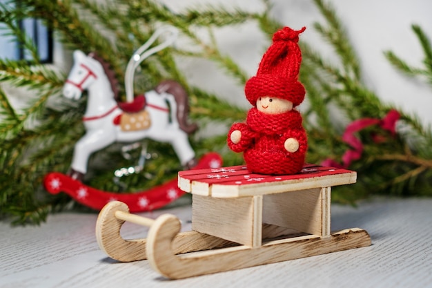 Criança de brinquedo vermelho brilhante em roupas de malha no trenó do papai noel com árvore de natal e um cavalo de brinquedo.