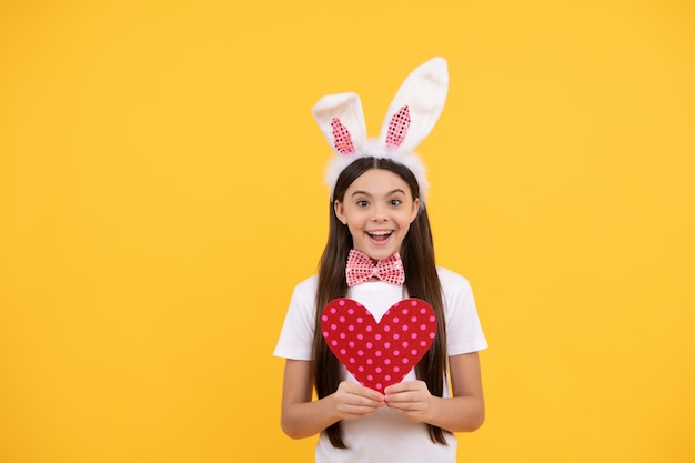 Criança de coelho alegre com coração de amor feliz feriado de páscoa criança engraçada em orelhas de coelho menina adolescente sorridente na caça ao coelho de gravata borboleta começar a se divertir pronto para a festa infância feliz