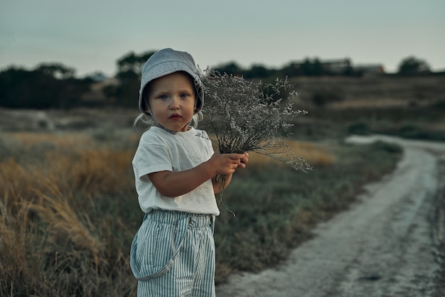 Criança de dois anos com chapéu caminhando por uma estrada rural