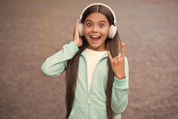 Criança de escola engraçada ouve música ou livro de áudio em fones de ouvido para educação e alegria vida moderna e diversão