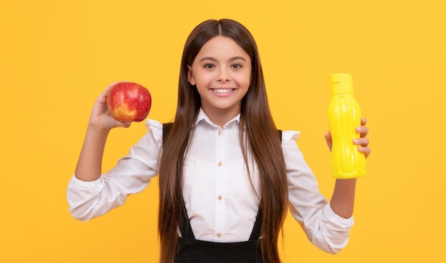 Criança de escola feliz de uniforme segura maçã e garrafa de água infância