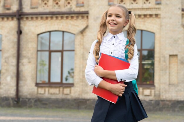 Criança de escola feliz em uniforme de volta à escola carregando livros e espaço de cópia de mochila