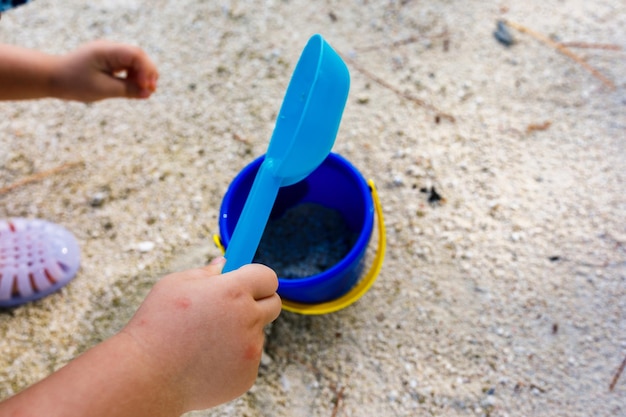 Criança de férias na praia pegando areia em um balde