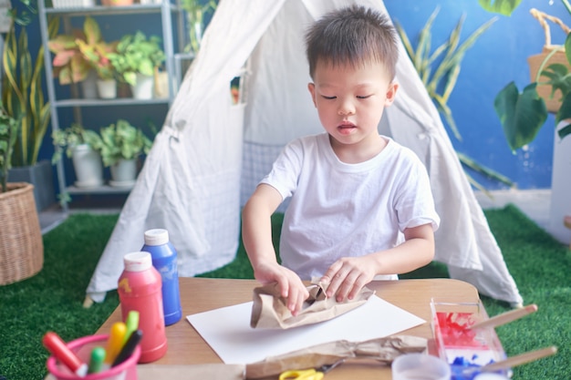 Criança de jardim de infância asiática de 4 anos de idade gosta de fazer artes e ofícios em casa, brinquedos DIY para crianças a partir do conceito de materiais recicláveis