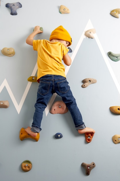 Criança de jeans e camiseta amarela escalando resolutamente a parede de escalada