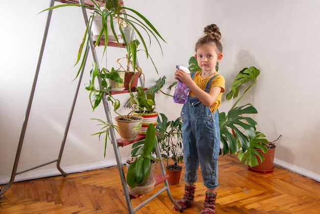 Criança de macacão jeans espirrandoxAhouseplantsxAin a estufa Garotinha cuida de plantas verdes na sala Jardinagem em casa amor por plantas e cuidados