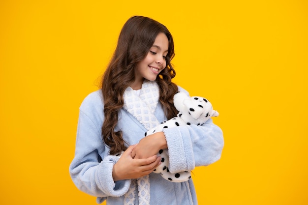 Criança de pijama bom dia menina adolescente segura brinquedo macio para aniversário em fundo amarelo criança com seus brinquedos