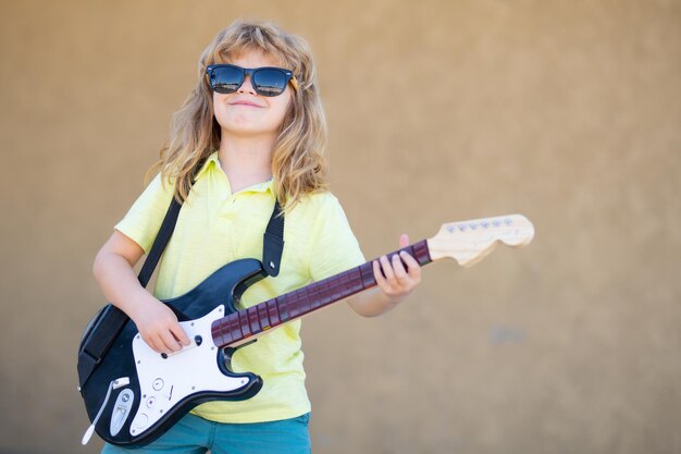 Criança de rock engraçada com guitarra Garotinho de óculos de sol Guitarrista de músico infantil tocando guitarra elétrica Conceito de música infantil