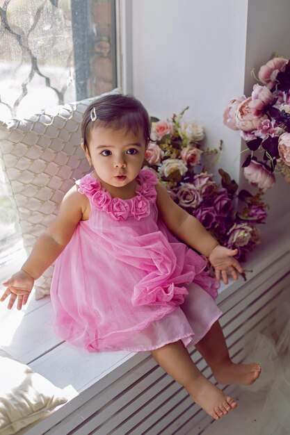 Criança de vestido rosa sentada na janela no peitoril branco