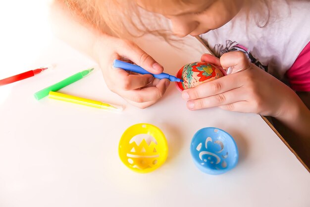 Criança decora ovos de páscoa com marcadores coloridos e modelos de plástico