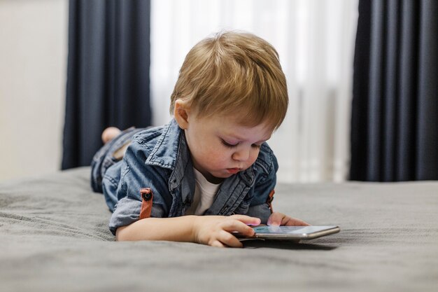 Foto criança deitada na cama usando telefone celular