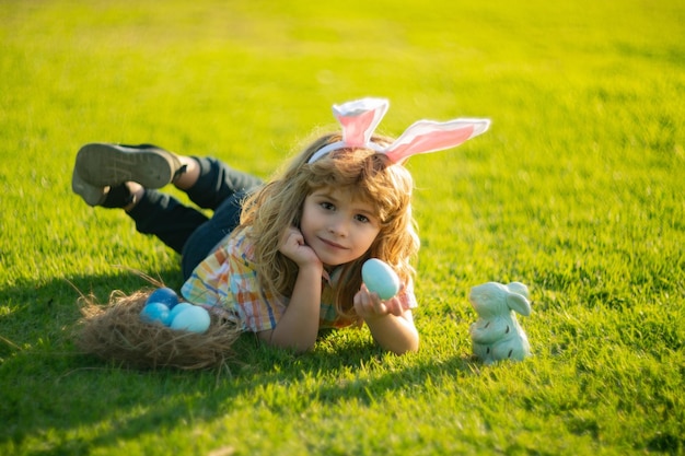 Criança deitada na grama no parque com ovos de páscoa criança menino caça ovo no dia de páscoa crianças ao ar livre pão de páscoa