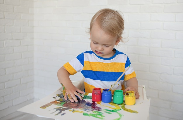 criança desenha com tintas, brincando em casa senta na mesa de uma criança brinquedos para criatividade