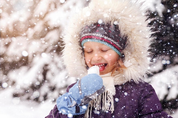 Criança Divirta-se no parque Snowy Winter. Bebê come neve fria, curtindo a vida. crianças no inverno