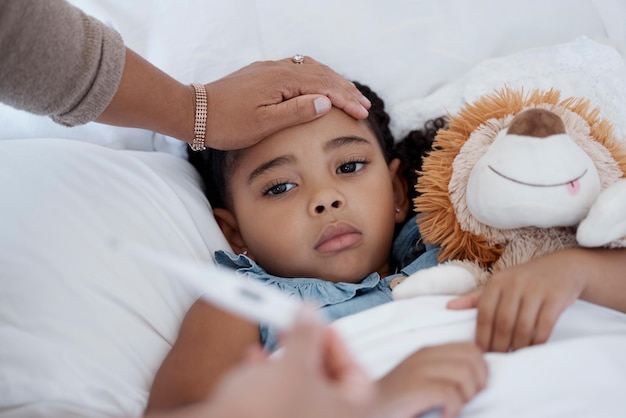 Foto criança doente covid e emergência médica na cama do problema de saúde em casa no quarto da casa e mãe com termômetro para febre mãe cuida de menina triste com vírus resfriado ou gripe no apartamento