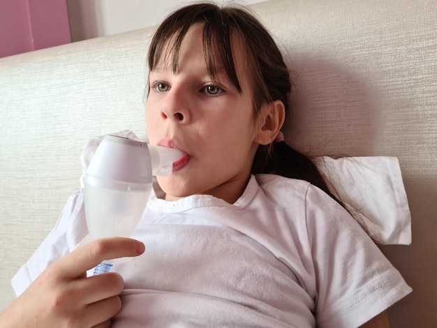 Criança doente deita na cama e faz inalações usando nebulizador