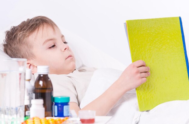 Criança doente deitada na cama com febre descansando em casa Criança enferma lendo um livro