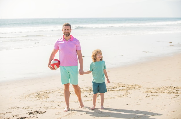 Criança e pai andando na praia nas férias de verão, segurando a bola, verão.