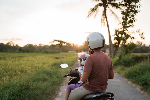 Criança e pai asiático andam de scooter de moto