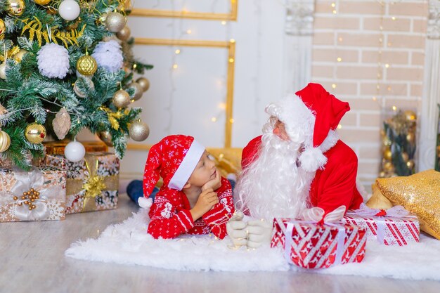 Criança e Papai Noel perto da árvore de Natal, menino olha para o Papai Noel