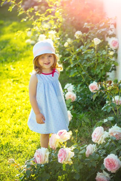 Criança em pé diante de flores rosas desabrochando na grama verde