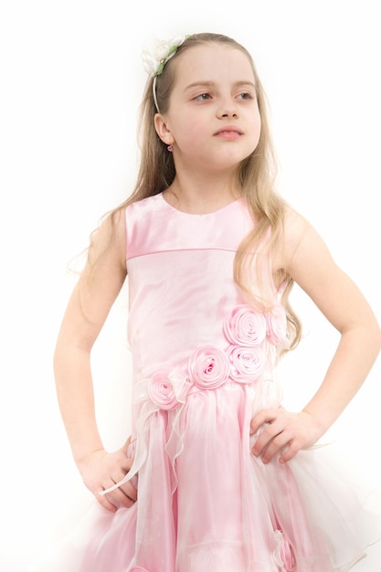 Criança em pose de vestido rosado isolada no branco. Moda, look, beleza e estilo. Garota com acessório de flor em longos cabelos loiros. Infância, flor, juventude. Inocência, conceito de pureza.