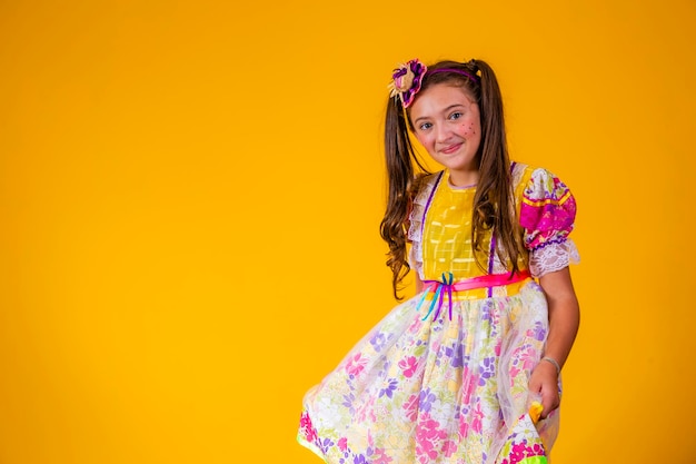 Foto criança em roupas típicas da famosa festa brasileira chamada festa junina em comemoração a são joão linda garota em fundo amarelo