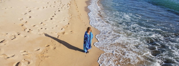 Criança em toalha andando na praia de verão