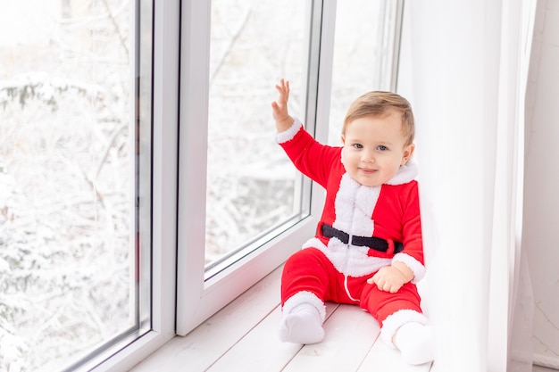 Criança em traje de Papai Noel no peitoril da janela, o conceito de ano novo e Natal