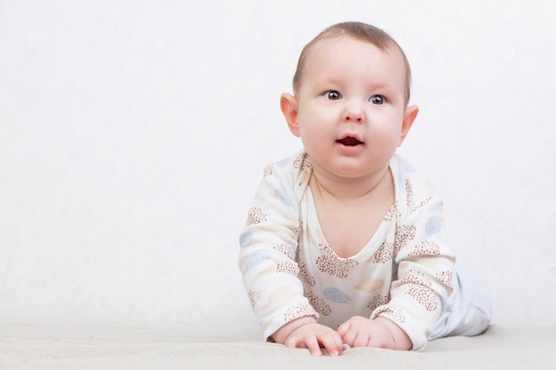 Criança em um fundo branco Um adorável bebê de seis meses está deitado na cama