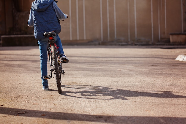 Criança em uma bicicleta na estrada de asfalto em dia ensolarado de primavera. Vista traseira