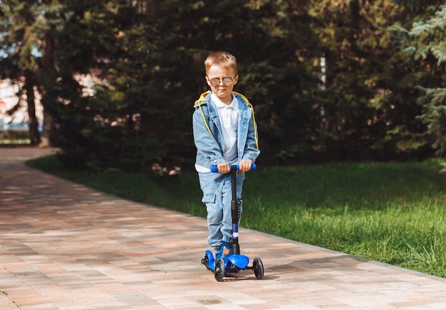 Criança em uma scooter no parque Um garotinho anda de scooter em um dia ensolarado Esportes ativos para pré-escolares