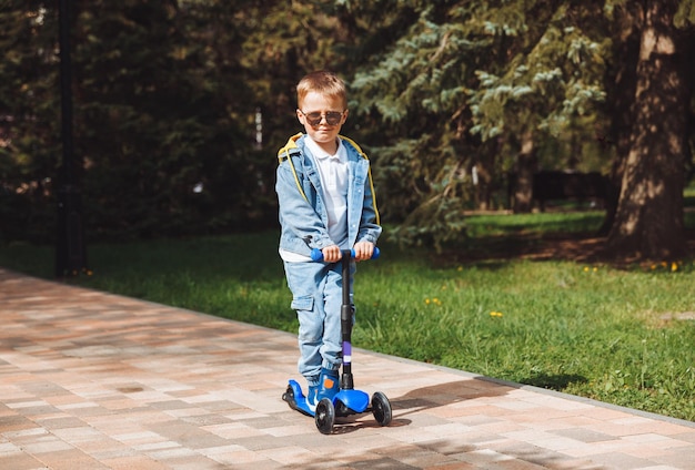 Criança em uma scooter no parque Um garotinho anda de scooter em um dia ensolarado Esportes ativos para pré-escolares