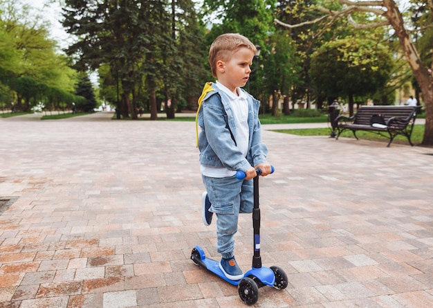 Criança em uma scooter no parque Um garotinho anda de scooter em um dia ensolarado Esportes ativos para pré-escolares