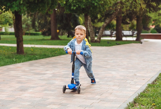 Criança em uma scooter no parque Um garotinho anda de scooter em um dia ensolarado Esportes ativos para pré-escolares