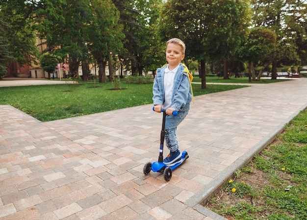 Criança em uma scooter no parque Um garotinho anda de scooter em um dia ensolarado Esportes ativos para pré-escolares