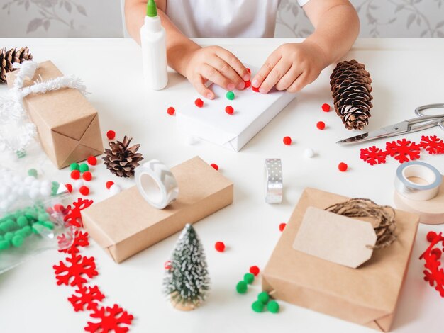 Foto criança embrulha presentes de natal em papel de artesanato com decorações presentes para a celebração do ano novo