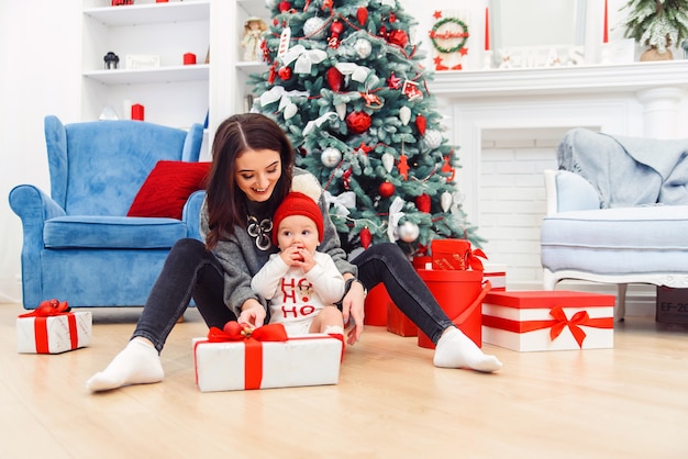 Criança encantadora com a mãe, desembalando o presente de Natal.