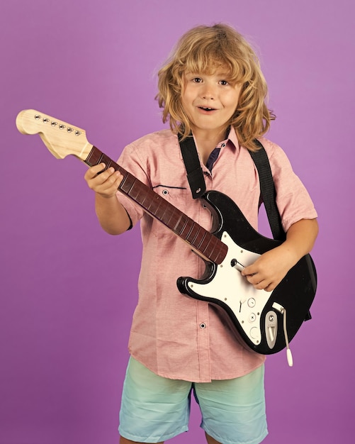 Foto criança engraçada com cabelo loiro e encaracolado tocando guitarra em um fundo isolado de estúdio menino caucasiano aprendendo a tocar guitarra