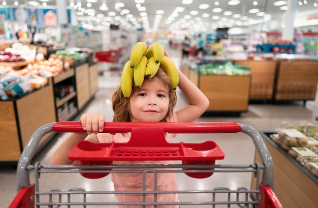 Foto criança engraçada com carrinho de compras comprando comida na mercearia ou no supermercado surpresa crianças com cara de banana