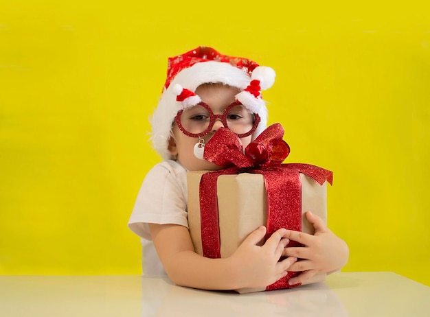 Criança engraçada com chapéu de Papai Noel vermelho tem o presente de Natal na mão. Conceito de Natal. Menino bonito no chapéu de Papai Noel. Bebê de ano novo em fundo amarelo.