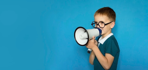 Foto criança engraçada em um fundo azul isolado grita no megafone para anunciar algo apontando para frente espaço para texto conceito de estilo de vida infantil