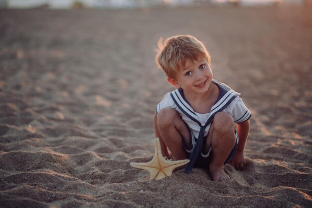 Foto criança engraçada está brincando na praia de areia menino feliz crianças férias férias em família a criança sorri e brinca com uma estrela-marinha praia férias oceano pôr do sol luz no mar