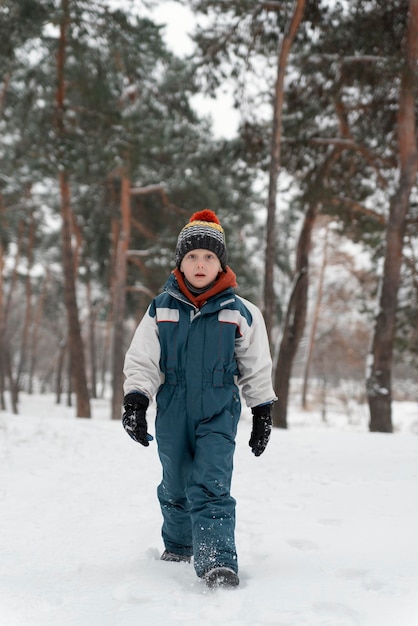 Criança engraçada fica na floresta de neve e olhando para a câmera Menino fica contra a bela paisagem de inverno